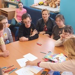 Autorka, nauczyciele i uczniowie siedzą przy stole z książkami i ilustracjami.