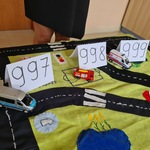 Na makiecie stoją samochody i kartki z numerami alarmowymi.