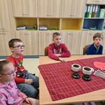 Uczniowie siedzą przy stole, przed nimi stoją filiżanki i pojemniki z herbatą.