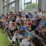 Nauczycielka w przebraniu smerfa mówi przez mikrofon do uczniów i nauczycieli siedzących na trybunie.