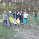 Grupa uczniów z workami na śmieci stoi na ścieżce w lesie.