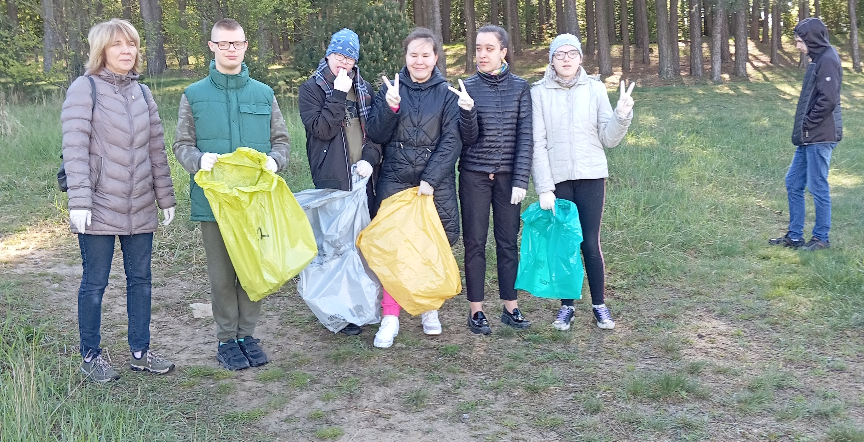 Grupa uczniów z workami na śmieci stoi na ścieżce w lesie.