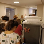 Grupa uczniów mija stojący na korytarzu wózek hotelowy z bielizną pościelową.