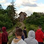 Grupa ludzi idzie ścieżką w kierunku drewnianej budowli.