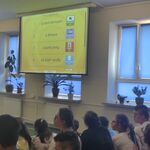 Uczniowie siedzą na ławeczkach i patrzą na ekran z wyświetlanym slajdem.