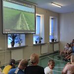 Uczniowie siedzą na łąteczkach i oglądają film wyświetlany na ekranie.