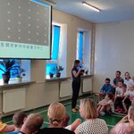 Nauczycielka omawia slajd wyświetlany na ekranie.  Wokół na ławeczkach siedzą uczniowie.