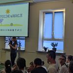 Nauczycielka omawia slajd wyświetlany na ekranie. Wokół na ławeczkach siedzą uczniowie.