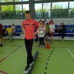 Uczeń idzie po równoważni. Z tyłu uczniowie obserwujący konkurencje sportowe.