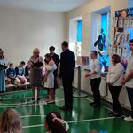 Społeczność szkolna patrzy na wręczanie przez panią dyrektor dyplomu absolwentowi.