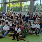 Uczniowie i nauczyciele siedzą na trybunach.