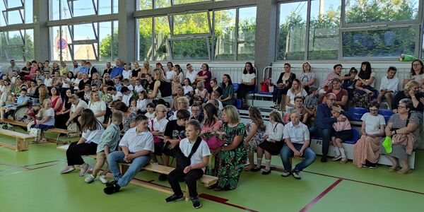 Uczniowie i nauczyciele siedzą na trybunach.
