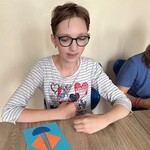 Uczennica siedzi przy stoliku, przed nią leży praca plastyczna.