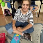 Uczennica siedzi na dywanie, przed nią leży praca plastyczna.