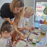 Uczennice i opiekunka wyklejają ziarnami formę.