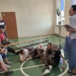 Uczniowie podczas zabawy w kałużę leżą na podłodze, w tle uczniowie i nauczyciele.