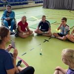 Grupa uczniów i nauczycielka siedzą w kole na podłodze.