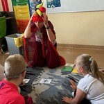 Uczniowie obserwują nauczyciela przebranego na czerwono zakładającego owocową czapkę.