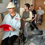 „Autobus”: nauczycielka i uczniowie siedzą w rzędzie na krzesłach.