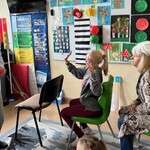 Nauczyciel przebrany za kierowcę siedzi na krześle. Za nauczycielem siedzą uczniowie.