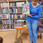 Pani bibliotekarka pokazuje uczniom siedzącym na podłodze książkę.