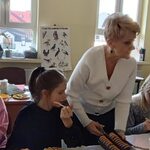 Nauczycielka stoi pomiędzy uczennicami siedzącymi przy urodzinowym stole.
