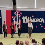 Nauczycielka prowadząca apel i czwórka uczniów ze sztandarami.