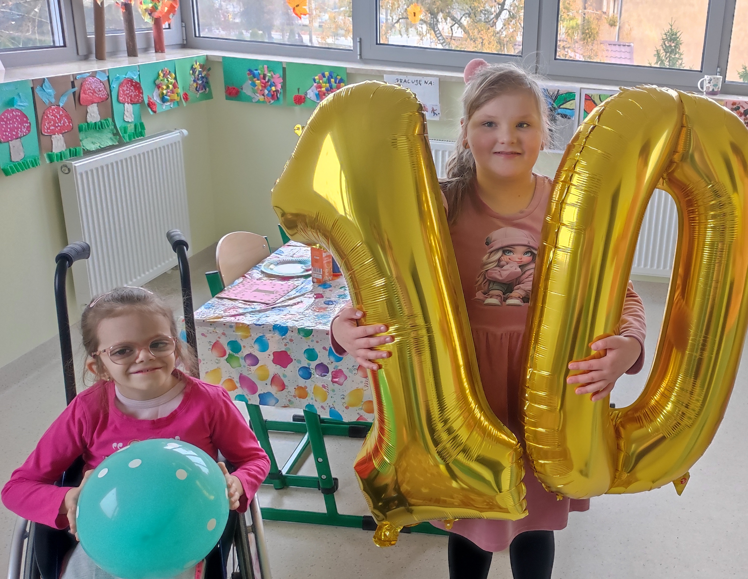 Jubilatka z balonami cyfr 1 i 0 stoi pomiędzy koleżankami.