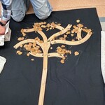 Na czarnym materiale drzewo zrobione z drewnianych klocków obsypane suchymi liśćmi.