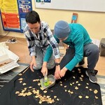 Uczeń zamiata miotełką suche liście. Nauczyciel pomaga uczniowi trzymać szufelkę.