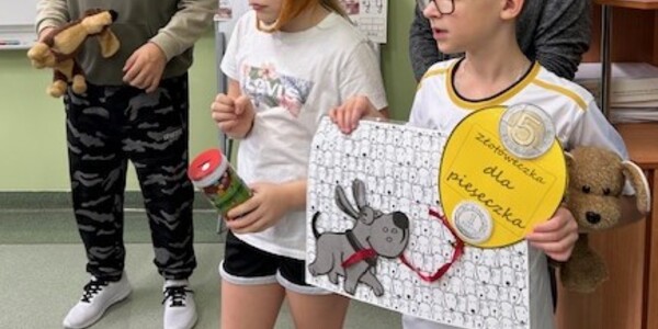 Uczniowie stoją z puszką na monety i z plakatem, na którym jest pies i hasło „Złotóweczka dla pieseczka”.
