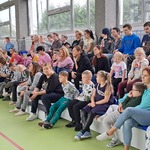 Społeczność szkolna siedzi na trybunie na sali gimnastycznej