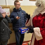 Mikołaj trzyma pudełko z batonikami, uczniowie rozpakowują batoniki.