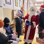 Mikołaj podaje cukierka uczniowi ubranemu w kurtkę.