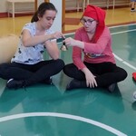Uczniowie i nauczycielka siedzą w kręgu. Uczennice podają sobie dzwonek.