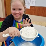 Uczennica przysypuje mąkę przez sito do miski.