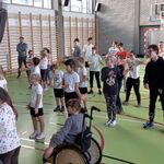 Grupa uczniów na sali gimnastycznej wykonuje ćwiczenia prezentowane na ekranie podczas lekcji online.