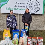 Dwoje uczniów stoi  na tle  logo schroniska..Przed uczniami w workach karma dla psów.