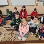 Grupa uczniów siedzi na dywanie.