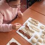 Uczennica maluje farbami karnawałowe smakołyki z masy solnej.