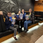 Uczniowie z pudelkami popcornu siedzą przy stoliku oczekując na seans filmowy.