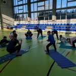 Na sala sportowej nauczycielka i uczniowie wykonują ćwiczenia gimnastyczne na matach.