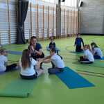 Na sala sportowej nauczycielka i uczniowie wykonują ćwiczenia gimnastyczne na matach.
