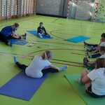 Na sala sportowej nauczycielka i uczniowie wykonują ćwiczenia gimnastyczne na matach.