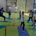 Na sala sportowej nauczycielka i uczniowie wykonują ćwiczenia gimnastyczne na matach.