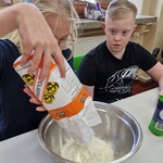 Uczennica wsypuje mąkę do miski