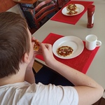 Uczeń siedzi przy stole na którym stoi talerz pizzerinką