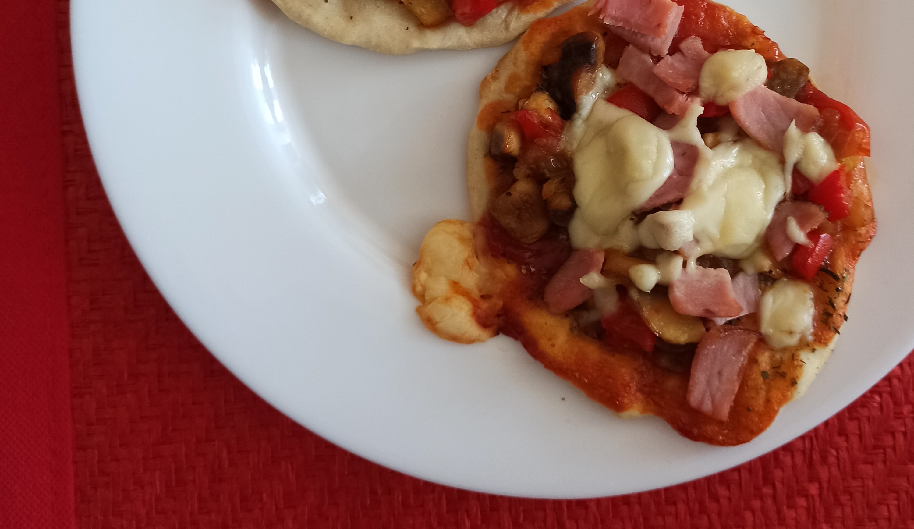Na czerwonej podkładce stoi talerz z dwiema pizzerinkami