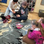 Nauczyciel i uczeń siedzą na podłodze. Nauczyciel trzyma ucznia za rękę tłumacząc mu polecenie