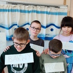 Uczniowie z kartkami przypiętymi do ubrań na tle płótna stojącego na sztaludze